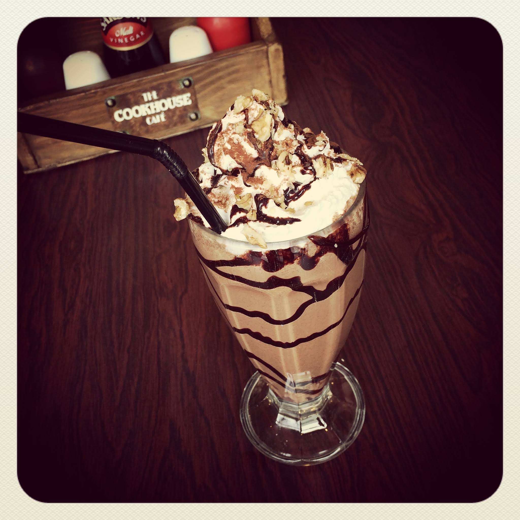 The Cookhouse Café milkshake in a complete glass with whipped topping and branded wooden caddy behind it